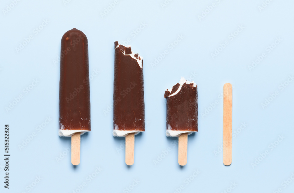 Chocolate covered ice cream on wooden stick consumption life cycle on blue background top view flat lay Chocolate covered ice cream on wooden stick consumption life cycle on blue background top view flat lay