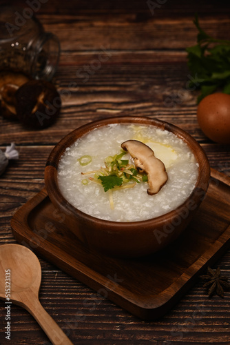 Delicious rice porridge with soft boiled egg, shiitake mushroom, slice ginger on wooden table for healthy breakfast