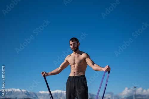 Shirtless man doing exercise with rubber bands outdoors. 