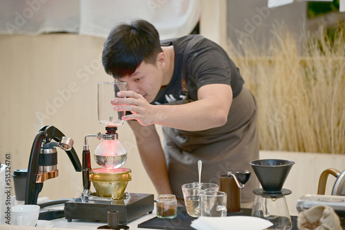 Closeup of Asian Male Barista using a coffee machine in a coffee shop to make coffee for customers to order inside a coffee shop cafe in Thailand.