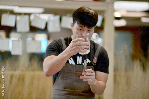 Closeup of Asian Male Barista using a coffee machine in a coffee shop to make coffee for customers to order inside a coffee shop cafe in Thailand. © masterjew