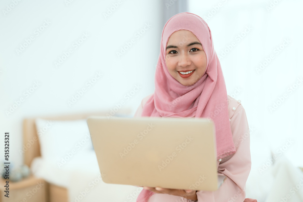 Muslim woman holding a laptop looking at the camera with a smile Muslim woman holding a laptop looking at the camera with a smile