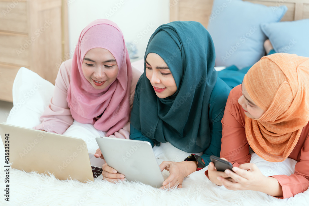 A group of Muslim women laying in bed chatting happily on their laptops. A group of Muslim women laying in bed chatting happily on their laptops.