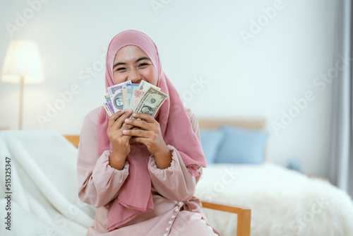 Muslim woman holding multi-currency money with smile. © 2B