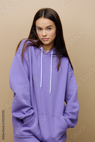 a beautiful, charming, attractive woman stands on a beige background in a purple tracksuit with her hands in the pockets of a hoodie © Tatiana