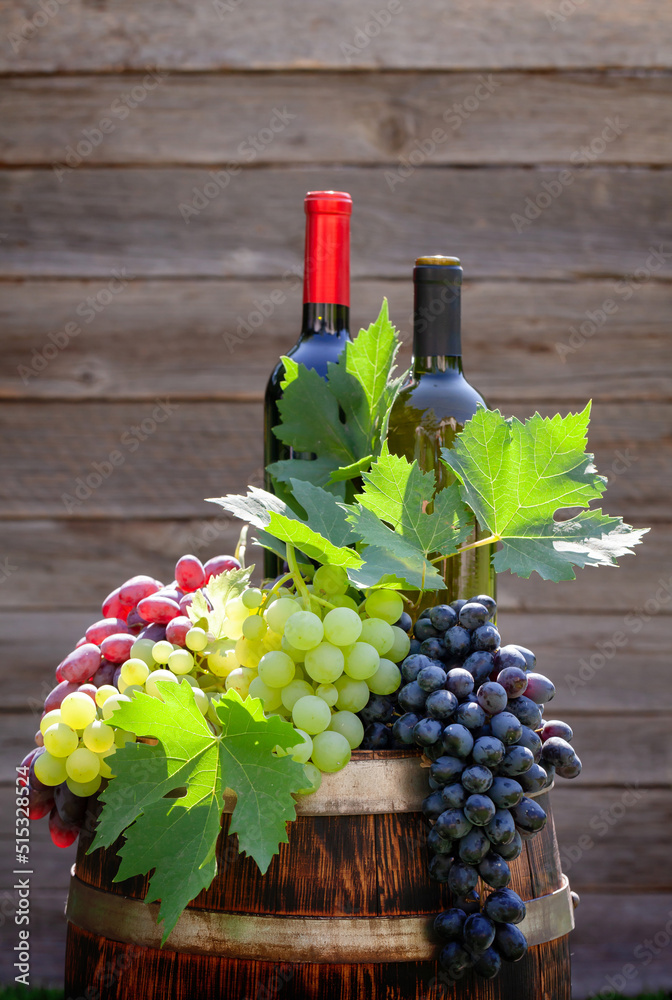 Various colorful grapes and wine bottles on wine barrel