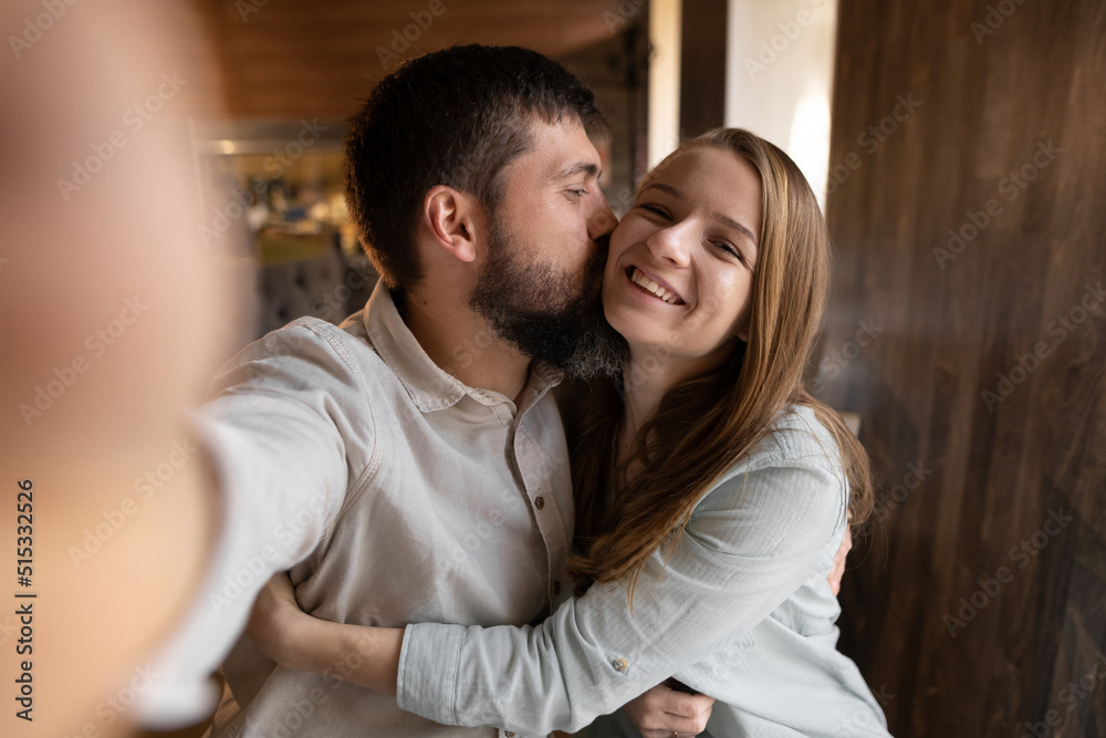 Smiling beautiful woman and her handsome boyfriend. Couple at their date in restaurant. Happy family. They taking Pov selfie at cafe and kissing