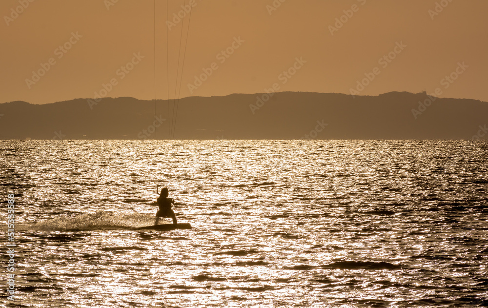 Expert Kitesurfer Planing with  Sea Watrer Splashes during Golden Hour in backlight on Blurred Background