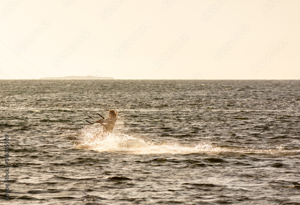 Expert Kitesurfer Planing with  Sea Watrer Splashes during Golden Hour in backlight on Blurred Background