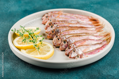Some fresh Black Sea red mullet on a white plate with lemon slices and thyme on a blue background.
