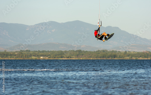 Expert Kitesurfer Jumping a Back Roll with Sea Watrer Splashes during Golden Hour