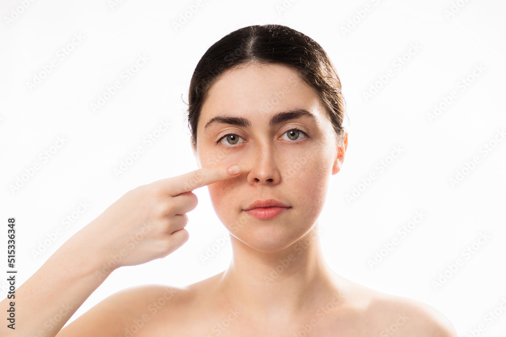 Plastic nose surgery. Portrait of young caucasian woman point her crooked bridge of the nose isolated on white background. Copy space. Concept of rhinoplasty Plastic nose surgery. Portrait of young caucasian woman point her crooked bridge of the nose isolated on white background. Copy space. Concept of rhinoplasty
