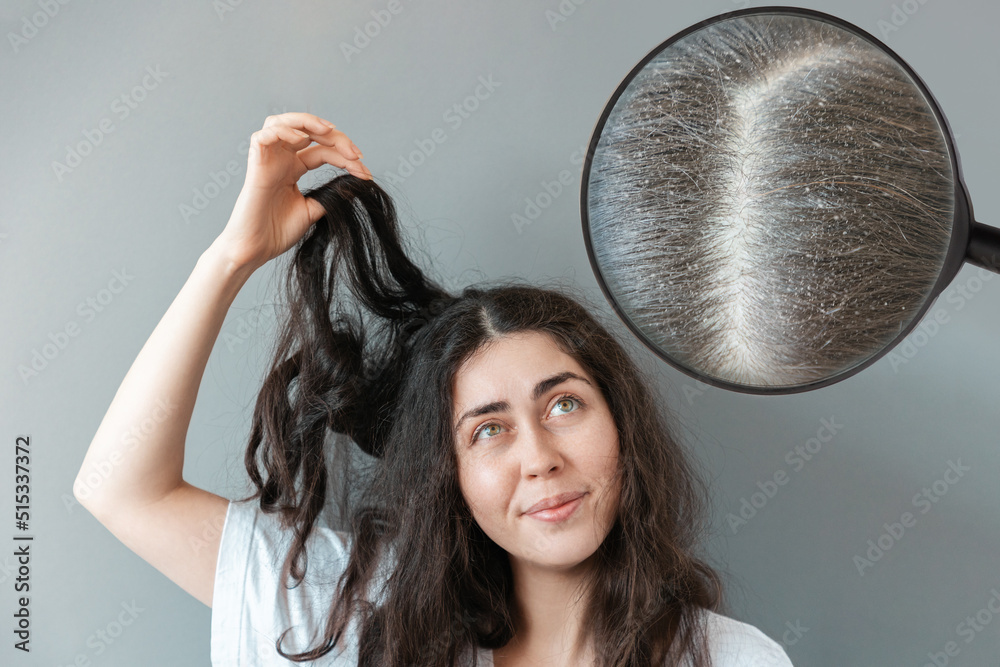 Young woman holds a tangled strand of her hair in bewilderment. Zoomed