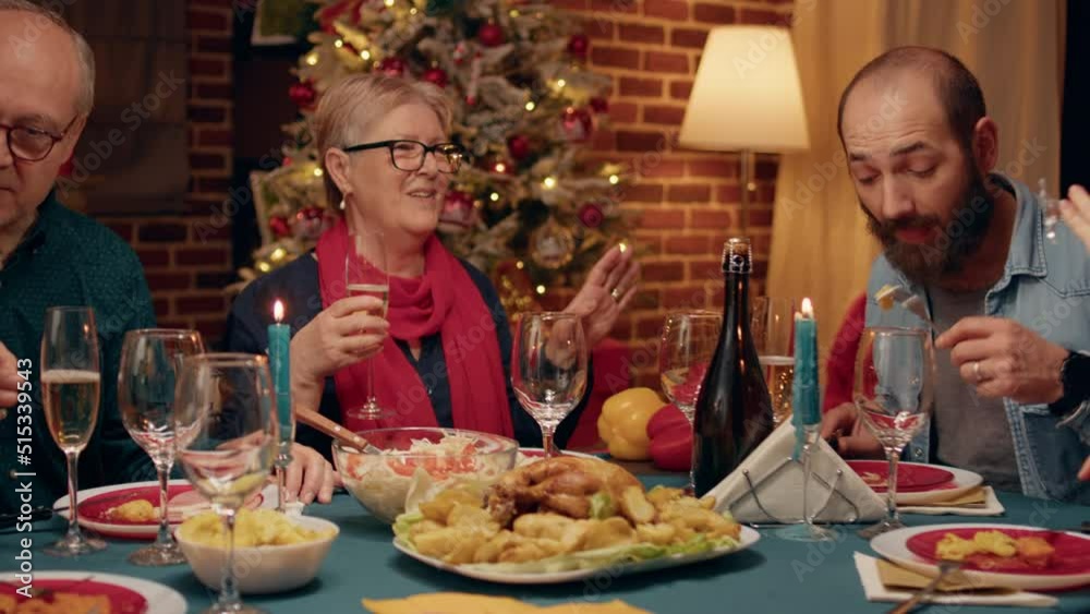 Festive diverse people clinking glasses while enjoying Christmas dinner table at home. Happy family members sitting in cozy apartment with Xmas decorations celebrating winter holiday together. Festive diverse people clinking glasses while enjoying Christmas dinner table at home. Happy family members sitting in cozy apartment with Xmas decorations celebrating winter holiday together.