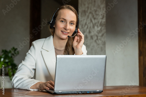 An attractive employee in a white jacket is sitting at her desk, holding a video conference with colleagues or clients. A woman with headphones, works as a call center operator.
