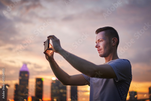Photography Man taking pictures via mobile phone of urban skyline at golden sunset, Singapore