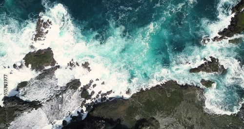 Aerial overhead shot sea waves hitting boulder and coral reef in the beach in sunny condition weather, the water looks blue and make white splash - Pengilon Hill, Indonesia, Asia photo