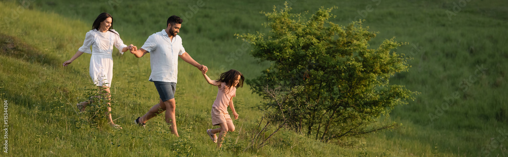 joyful family holding hands and running on green slope in countryside, banner. joyful family holding hands and running on green slope in countryside, banner.
