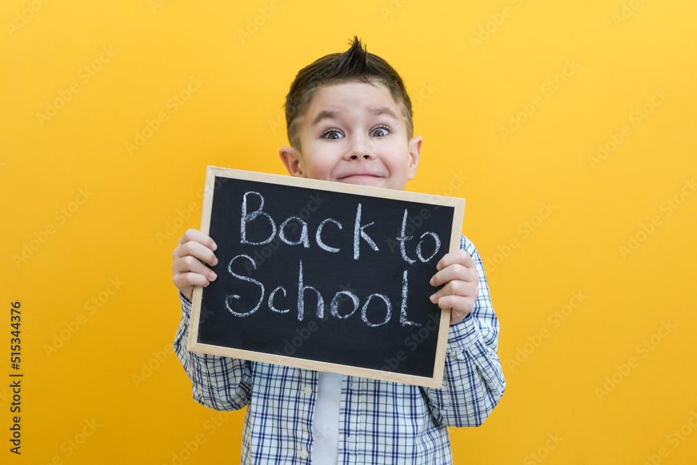 schoolboy holding a tablet in his hands with the inscription Back to school on a yellow background. schoolboy holding a tablet in his hands with the inscription Back to school on a yellow background.