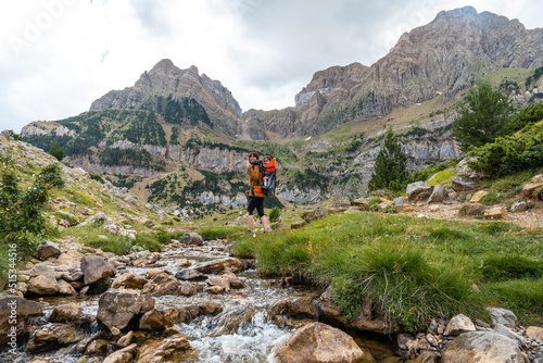 Woman with her son in the backpack walking in the Pyrenees in summer next to a river, Tena Valley