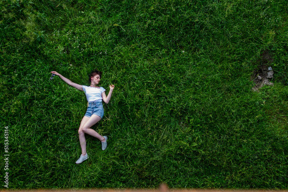 Portrait of happy cute young woman with short hair in casual black and white striped shirt, red round eyeglasses lying down on green grass and looking at camera through glasses.outdoor summertime shot Portrait of happy cute young woman with short hair in casual black and white striped shirt, red round eyeglasses lying down on green grass and looking at camera through glasses.outdoor summertime shot