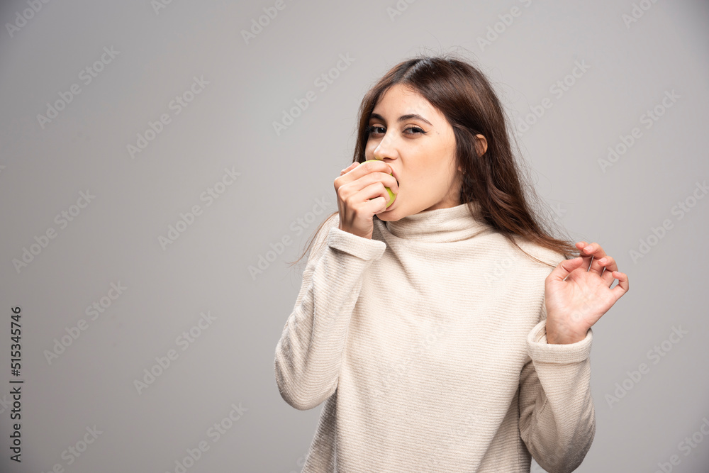 A young girl biting a green apple on a gray background A young girl biting a green apple on a gray background