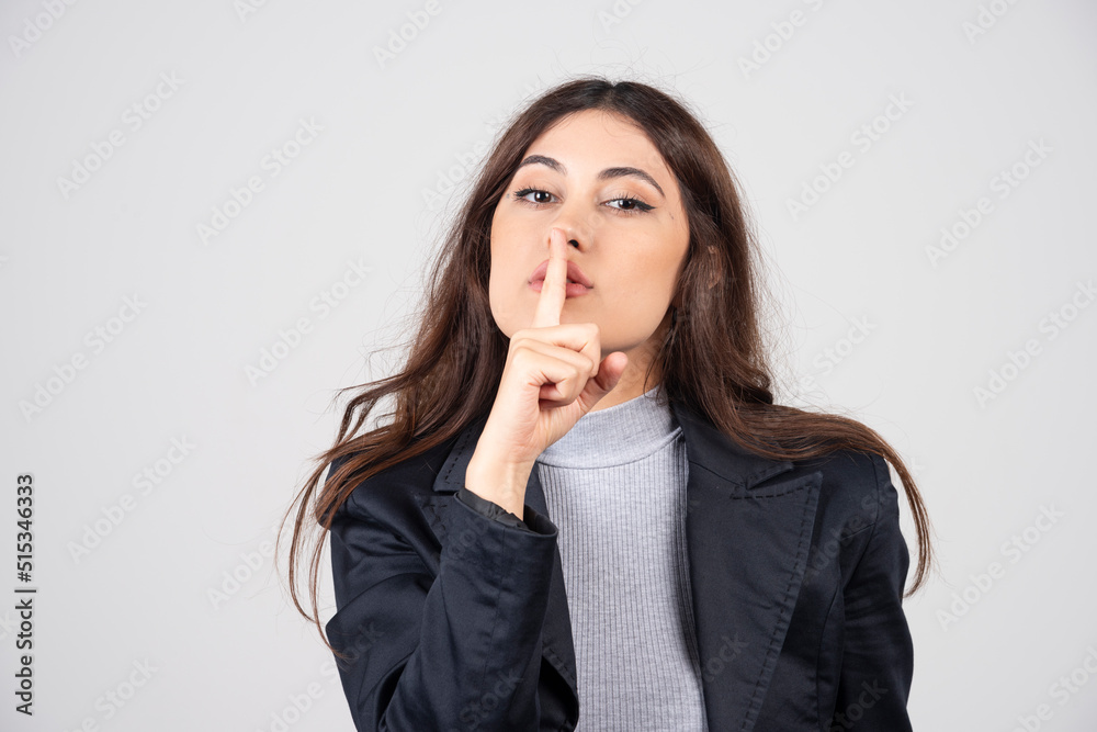 Young woman showing a sign of silence gesture putting finger in mouth Young woman showing a sign of silence gesture putting finger in mouth