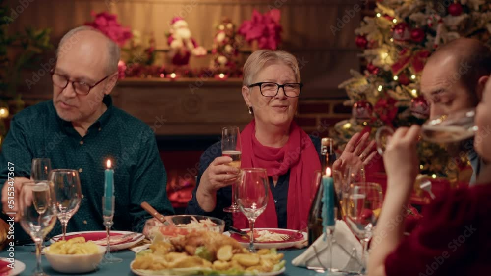 Happy elder woman clinking glasses with young person while enjoying Christmas dinner in family. Smiling senior person drinking champagne while celebrating winter feast with relatives. Happy elder woman clinking glasses with young person while enjoying Christmas dinner in family. Smiling senior person drinking champagne while celebrating winter feast with relatives.