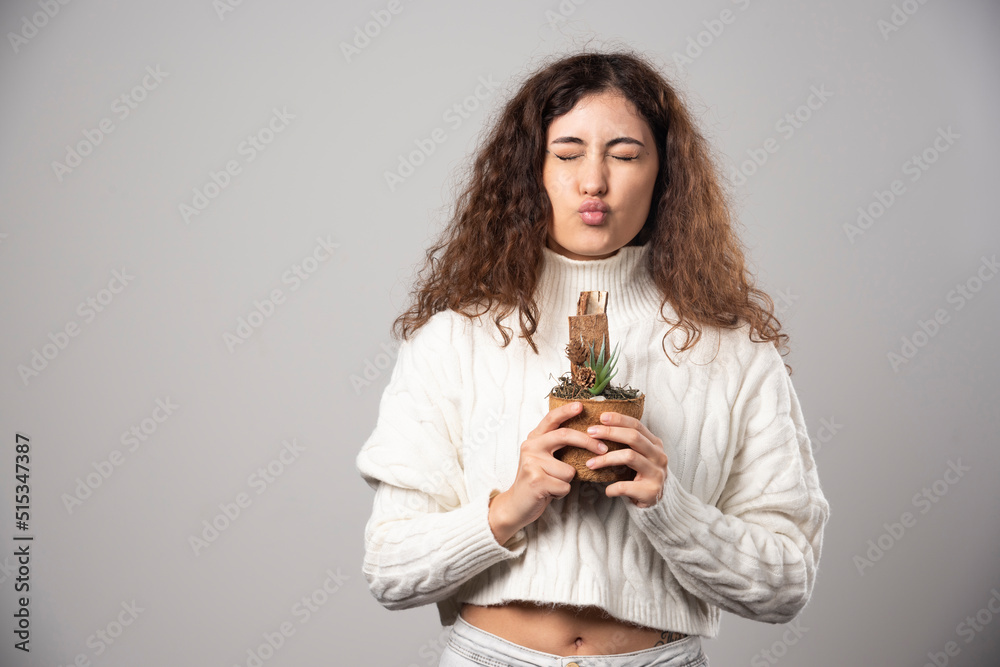 Young woman gardener holding a plant on a gray wall Young woman gardener holding a plant on a gray wall