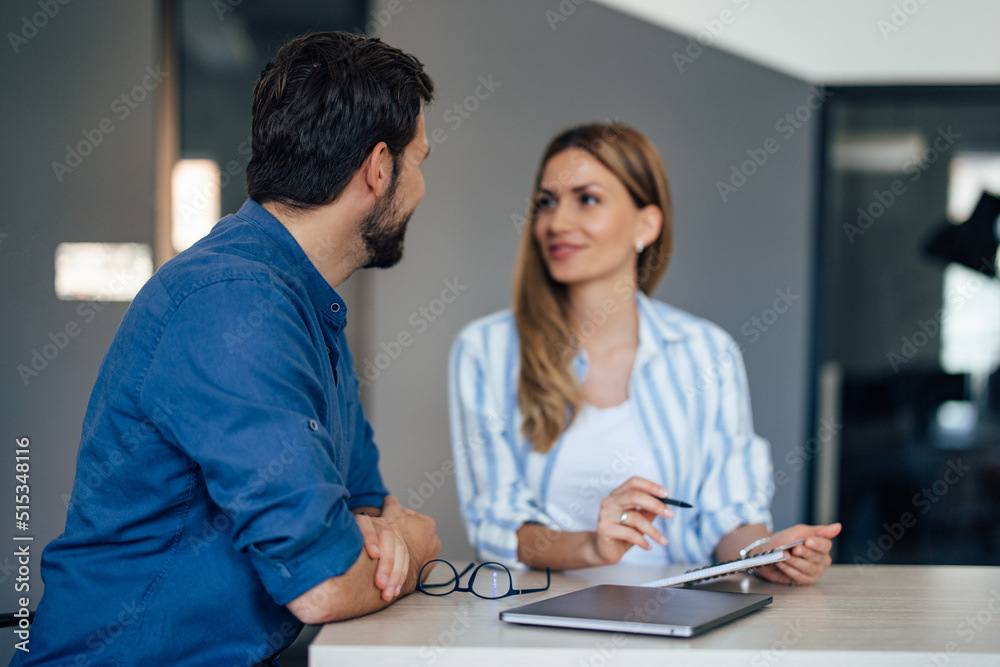 Blonde adult woman showing some notes to her male boss while looking at him. Blonde adult woman showing some notes to her male boss while looking at him.