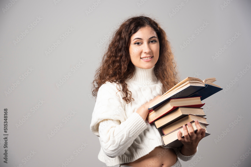 Young smiling woman carrying a lot of books on a gray wall Young smiling woman carrying a lot of books on a gray wall