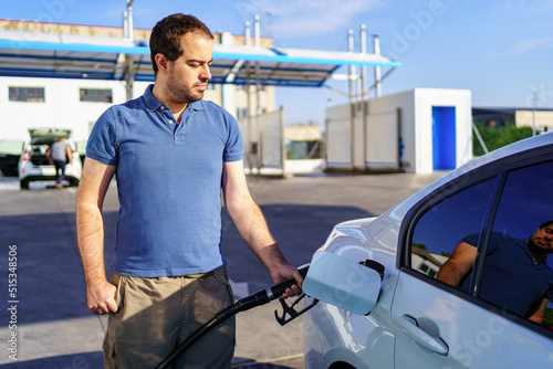 Caucasian young man refilling the tank of a fuel car at a gas station.