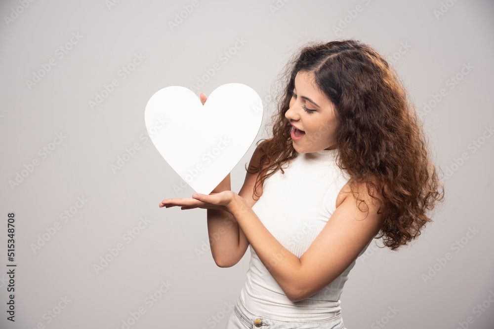 Young woman looking at white handmade paper heart Young woman looking at white handmade paper heart