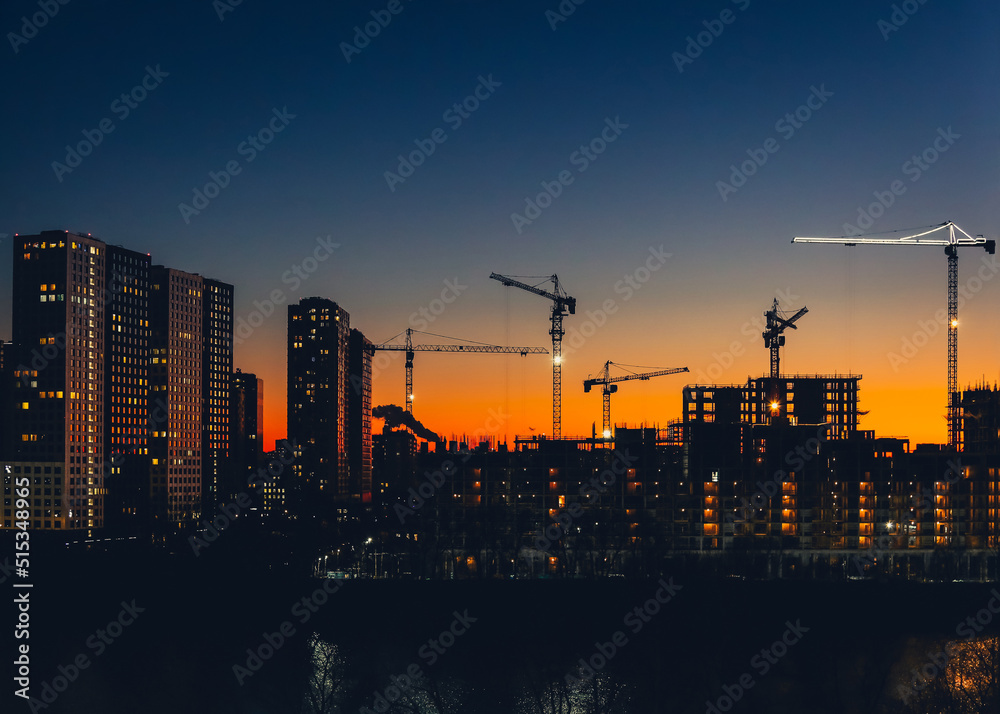 Naklejka premium Metropolitan skyline with tower cranes building high-rise residential buildings in evening time. Steel frame structure in sunlight. Industrial background. Lifestyle