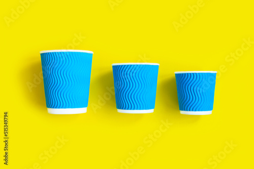 Blue paper cups of coffee or tea to go on bright yellow background. Eco friendly concept. Flat lay. Top view