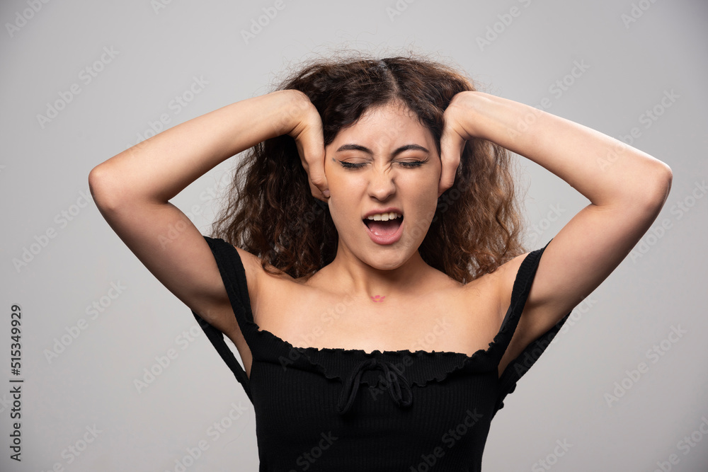 Young woman closing her ears in black blouse with curly hair Young woman closing her ears in black blouse with curly hair