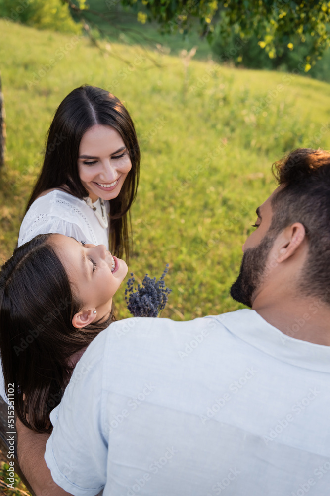 Fototapeta premium excited girl with lavender flowers laughing near happy parents outdoors.