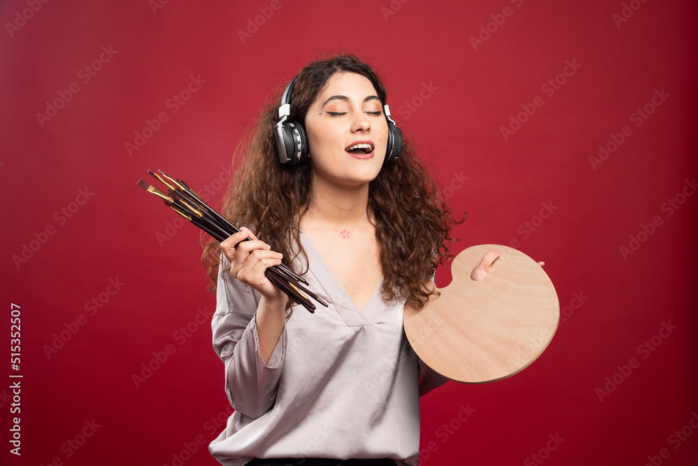 Woman in headphones holding palette and paintbrushes Woman in headphones holding palette and paintbrushes