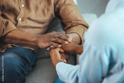 Close up black woman and man sitting on couch two people holding hands. Symbol sign sincere feelings, compassion, loved one, say sorry. Reliable person, trusted friend, true friendship concept photo