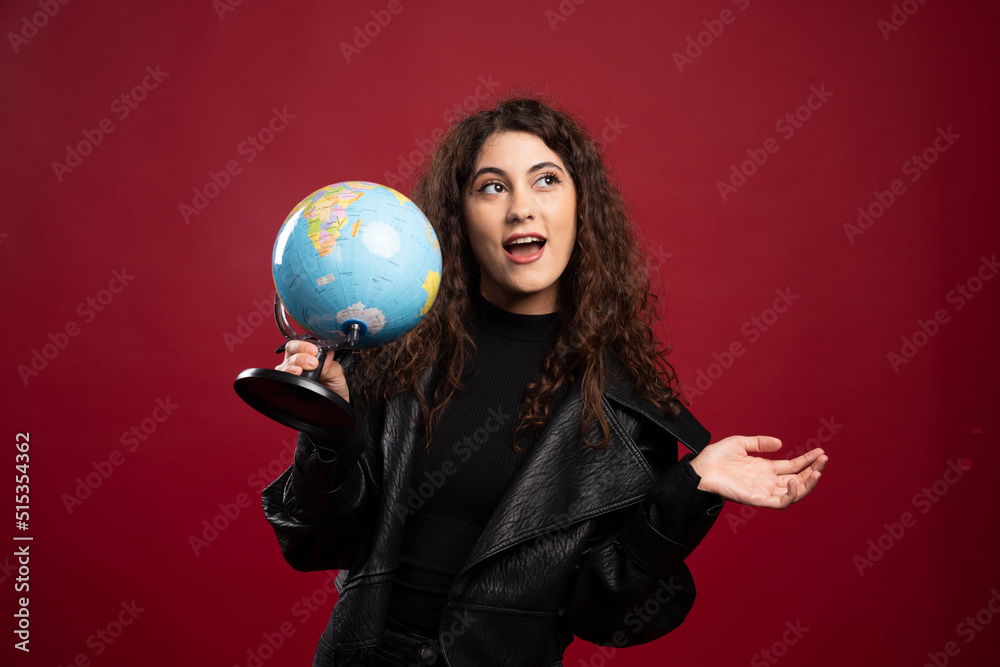 Naklejka premium Cheerful woman holding globe on red background