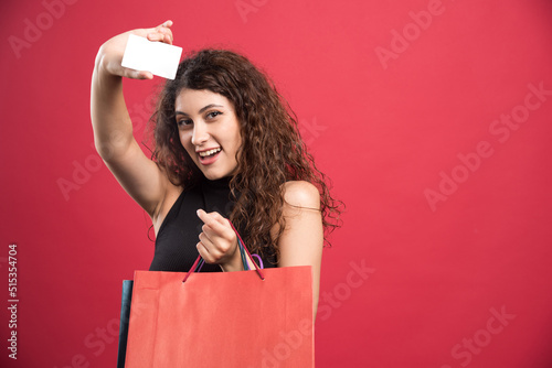 Happy woman with many of bags and bank card on red background