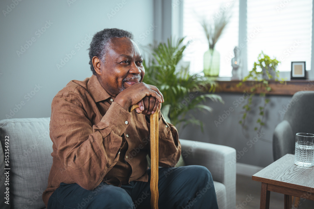 Portrait of a senior man sitting at home with a walking stick. Senior Afro-American with Walking Stick is Sitting in Comfortable Armchair 