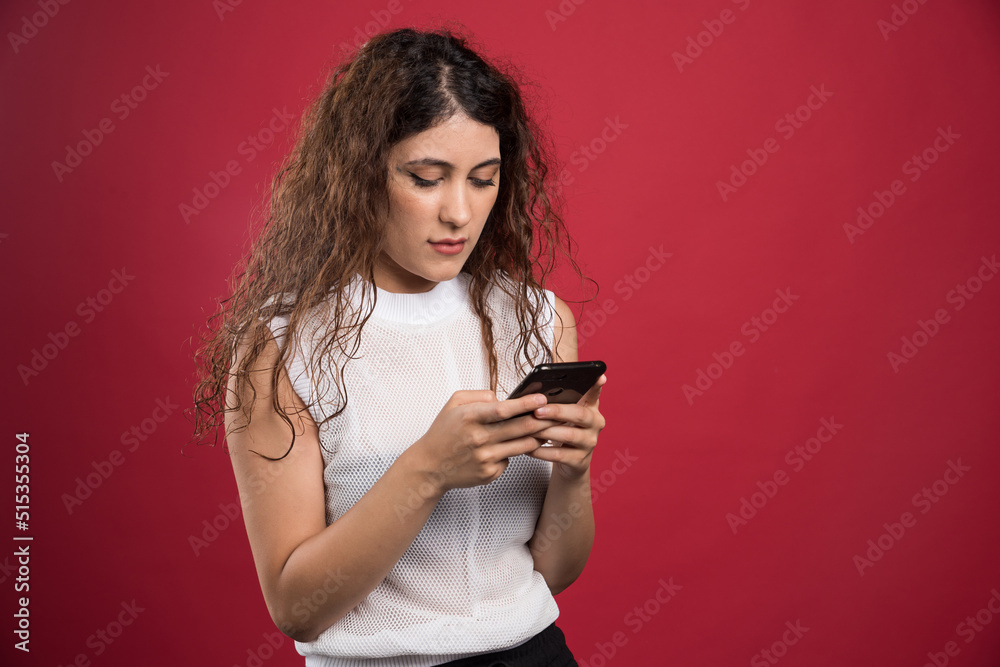 Surprised woman is typing something on her mobile phone on red background Surprised woman is typing something on her mobile phone on red background