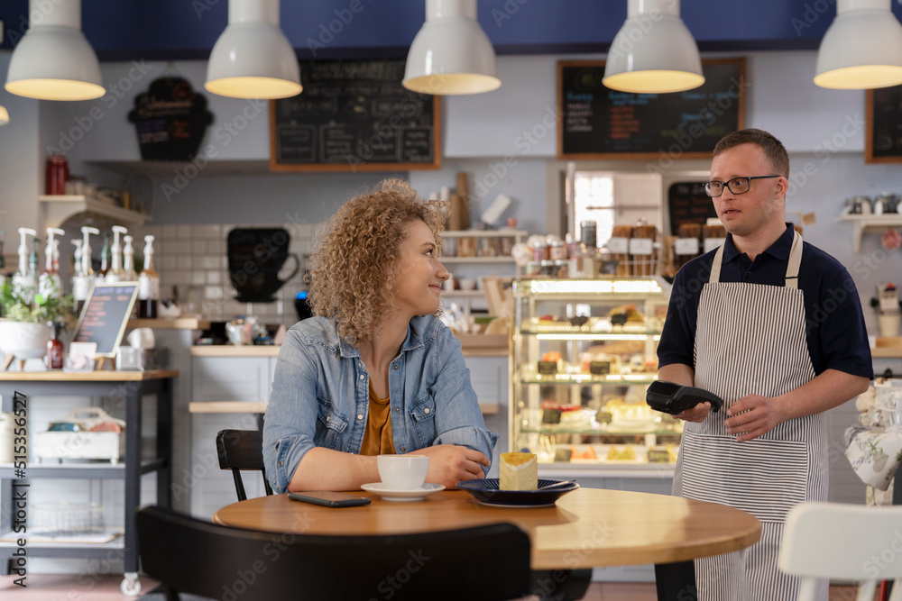 Caucasian man with down syndrome accepting contactless payment from the client at the table Caucasian man with down syndrome accepting contactless payment from the client at the table