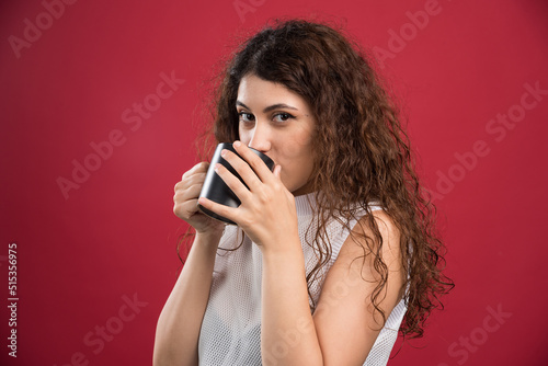 Woman drinking from dark cup on red background