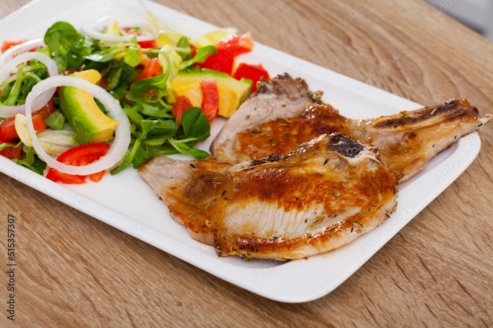 Two grilled pork rib chop steaks served with avocado, tomato, onion and corn salad