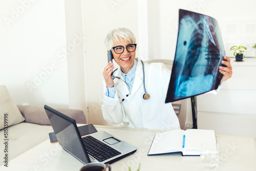 Women oncologist calling patient, informing about lung disease, x-ray examination. Doctor analysing X-ray image with her patient via smartphonr in consulting room. photo