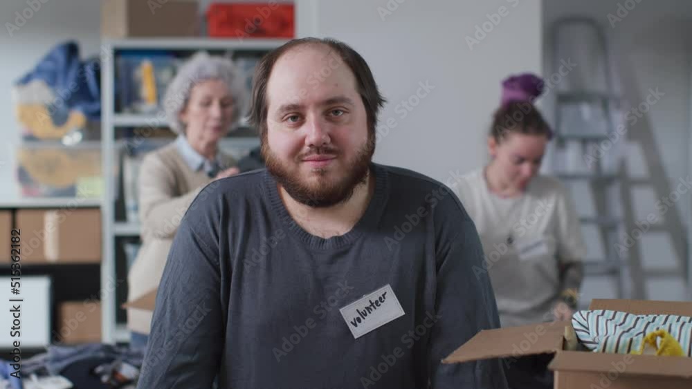 Alternative military civilian service. Portrait of overweight male volunteer smiling at camera working in military donation center with people packing donated clothes in boxes for humanitarian aid Alternative military civilian service. Portrait of overweight male volunteer smiling at camera working in military donation center with people packing donated clothes in boxes for humanitarian aid