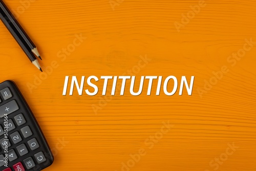 INSTITUTION - word (text) on a yellow wooden background, a calculator and a pencil. Business concept (copy space).