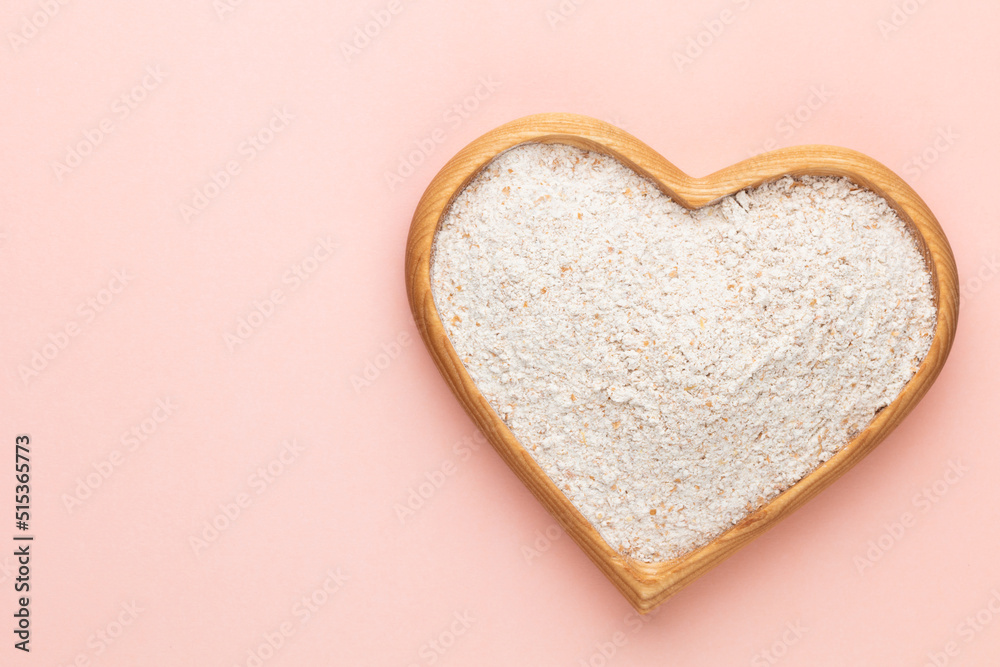 Wheat flour in a wooden heart shape bowl on a pastel background. Wheat flour in a wooden heart shape bowl on a pastel background.